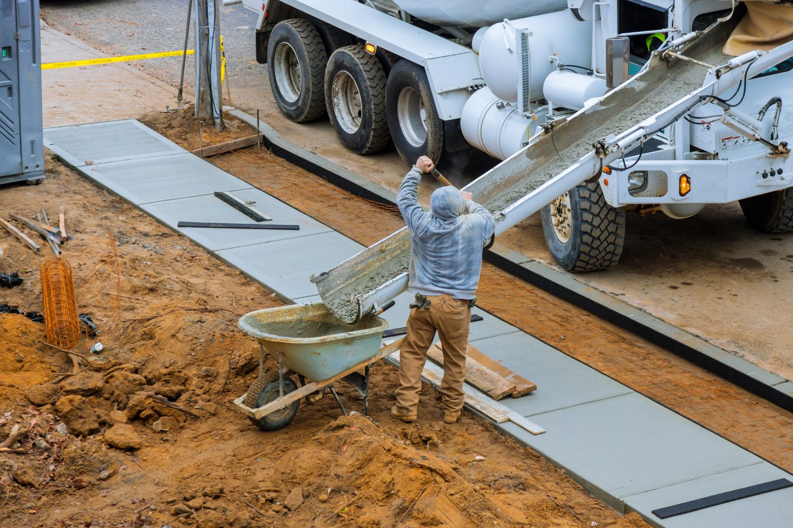 Construction worker pour cement for sidewalk in concrete works with mixer truck with wheelbarrow